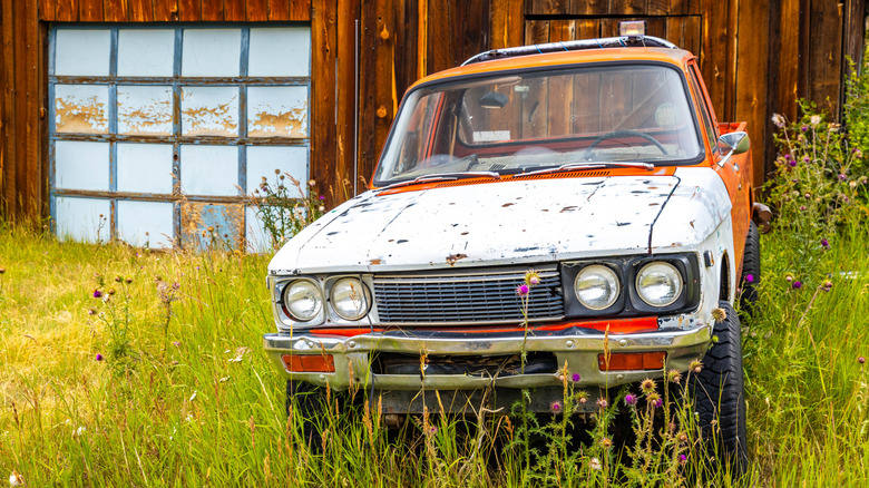 Rusted pickup truck in field in front of wooden barn
