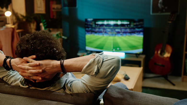 Rear view shot of a man watching football in a smart TV