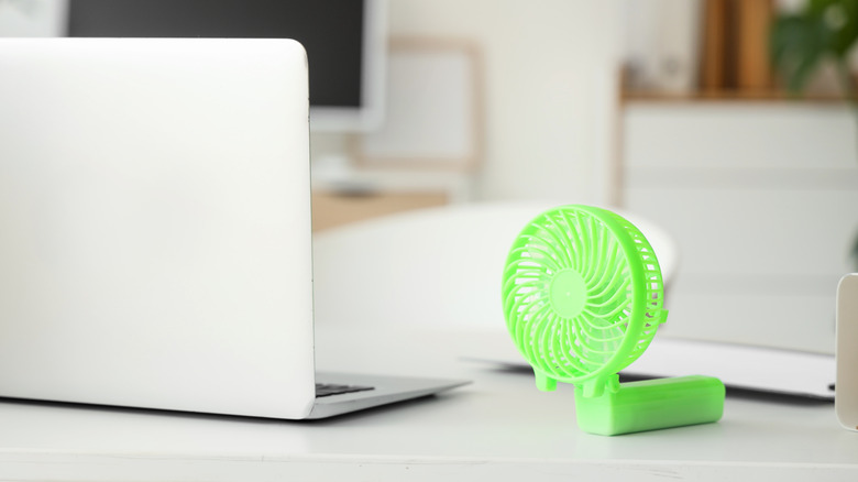 A fan on the table next to a laptop