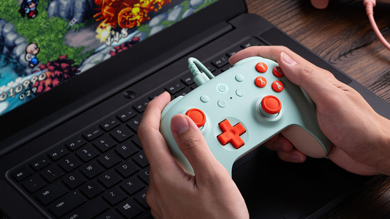 A person using a gaming controller with their laptop