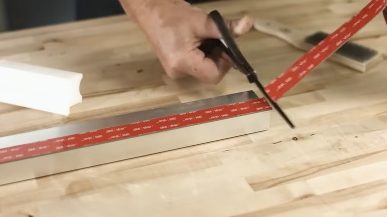 Person applying VHB tape with a pair of scissors on a wooden tabletop