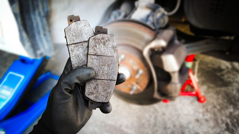 Gloved hand holding worn brake pads in front of vehicle brake assembly