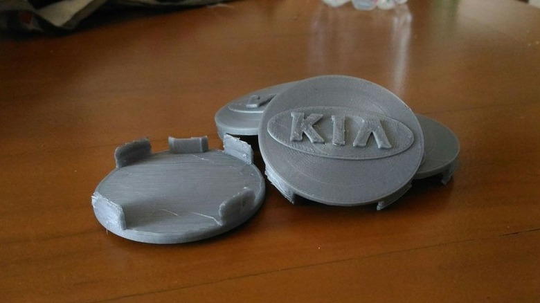 Four 3D printed Kia-labeled wheel caps on a wood surface