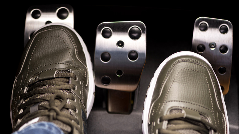 A close up of a driver's feet on the three pedals of a manual transmission car