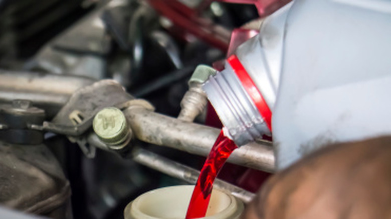 Close up of a mechanic pouring transmission fluid into an engine reservoir