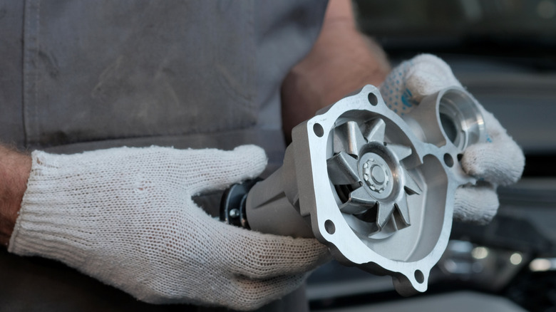 A close up of a replacement water pump in mechanic's hand