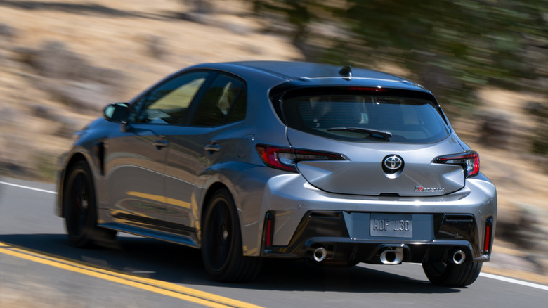 Rear 3/4 view of 2026 Toyota GR Corolla on winding road in forested area