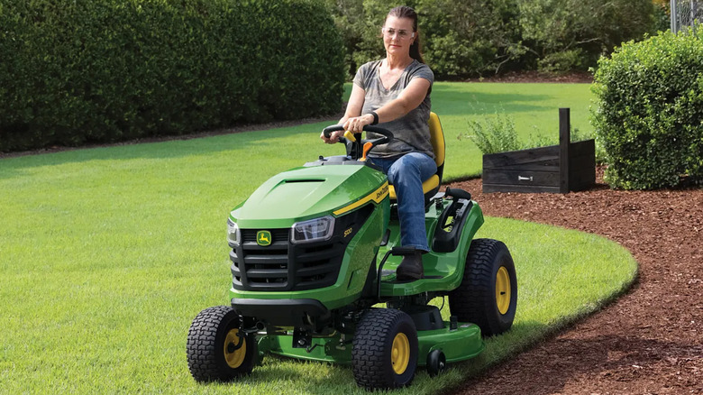 A woman riding a John Deere S120 riding lawn mower.