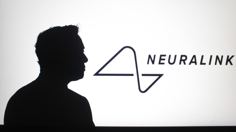 The silhouette of a man looking at the Neuralink logo projected onto a wall