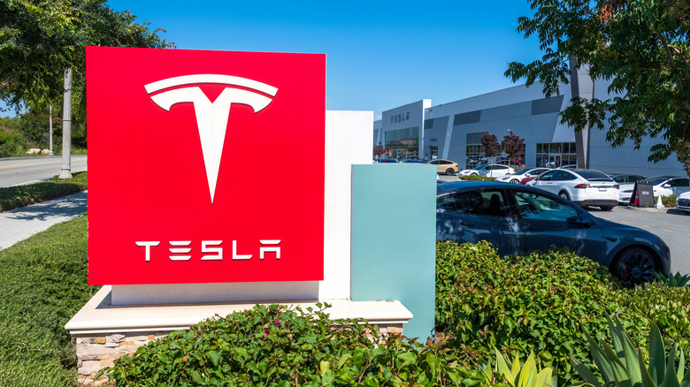 A Tesla sign on a decorative lawn outside a delivery fulfilment center