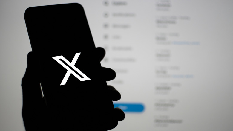 A hand holding a smartphone with the X, Formerly Twitter logo displayed on the screen