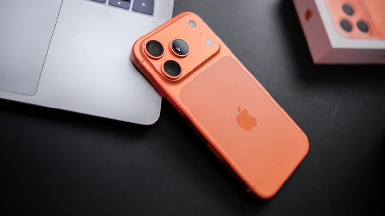 An orange iPhone lying on a MacBook, next to its box on a black surface