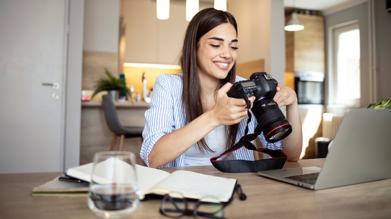 Woman holding DSLR camera and working on laptop