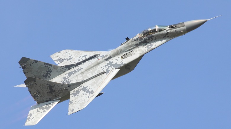 A MiG-29 with digital desert camo flying over blue skies