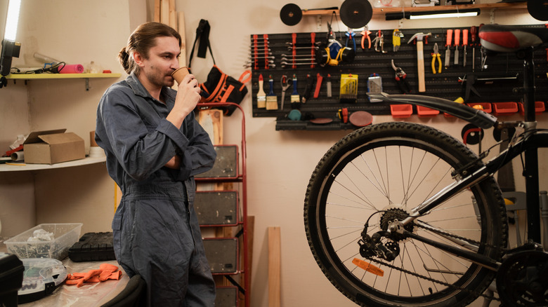 A man sipping coffee while he works on a bicycle in a garage