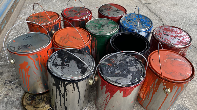 A dozen cans of different colored paint sitting on the ground