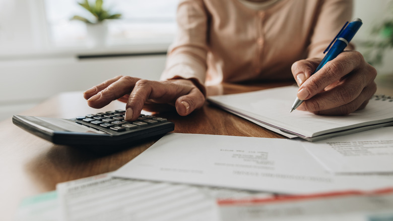 An older person doing calculations with a pen and calculator.