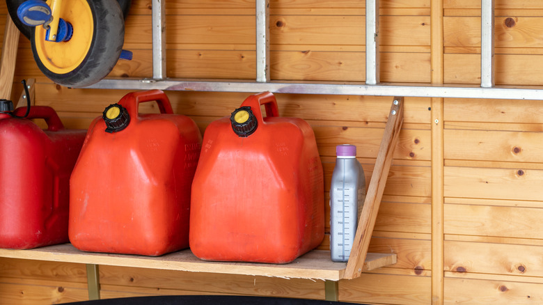 A row of jerry cans seated on an adjustable shelf in a garage.