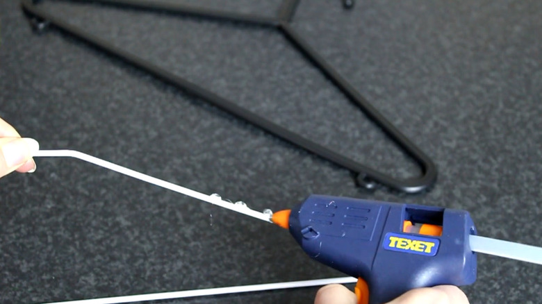 A person applying glue to a hanger with a glue gun
