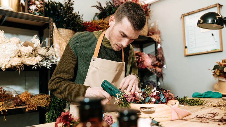 A florist using a glue gun to hold flowers in a vase