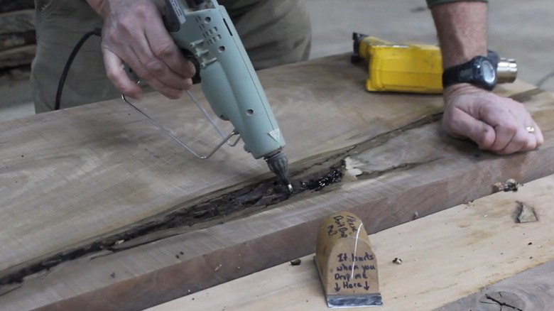 A person filling holes in wood with a glue gun