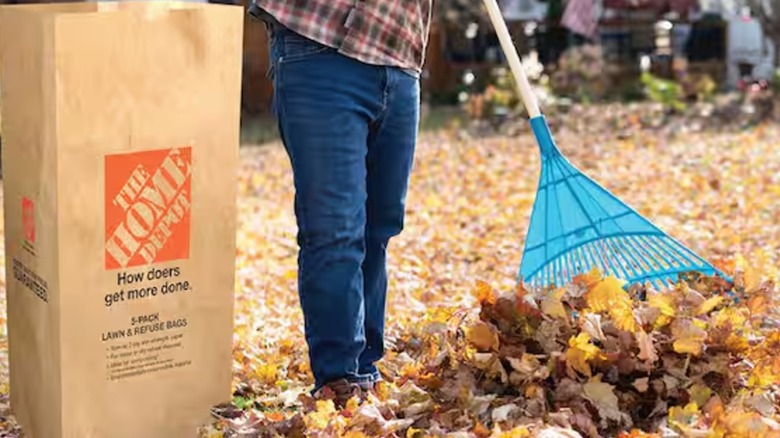A person raking leaves next to Home Depot bag