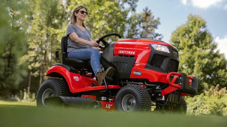 Woman using a Craftsman riding lawn mower on an inclined surface.