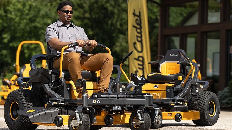 Man sitting on a riding lawn mower with another one parked beside.