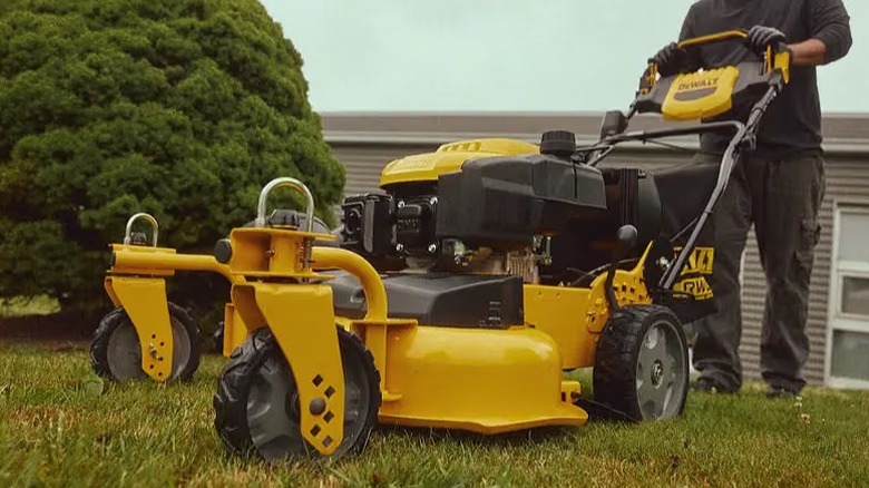 Man walking behind a yellow and black DeWalt lawn mower moving on grass.
