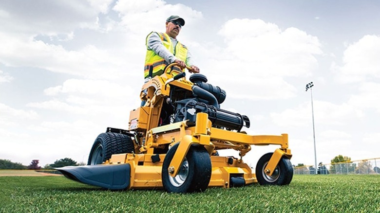 Worker using a Hustler riding lawn mower in a ground.