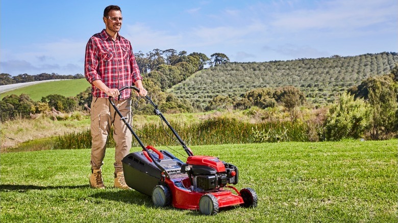 Man walking behind a lawn mower in an open field.