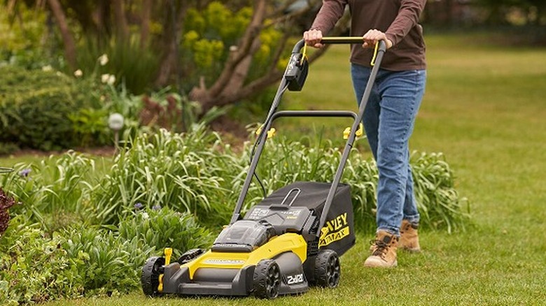 Woman walking behind a Stanley lawn mower in a garden.