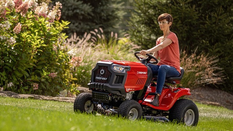 Woman riding a Troy-Bilt riding lawn mower up a steep surface.