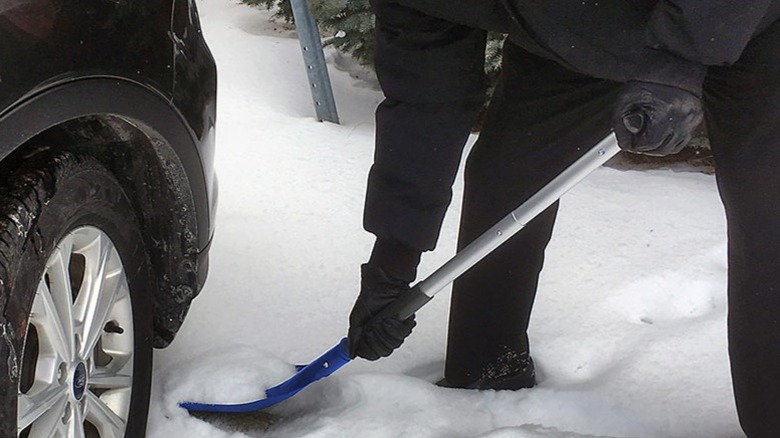 Close-up of a person shoveling snow next to a car tire using a Michelin snow shovel