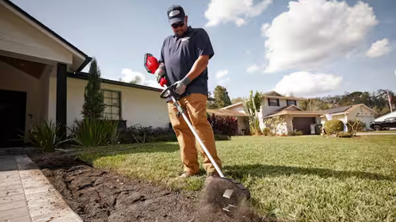A man using a cultivator to clear grass near a driveway