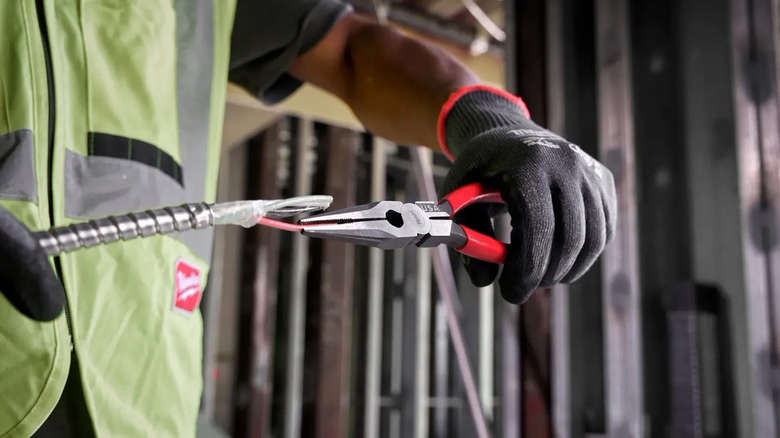 An electrician using needle nose pliers to grasp a wire