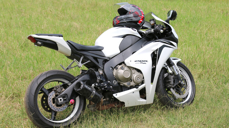 A white Honda CBR1000RR supersport motorbike parked on its kickstand on grass on a cloudy day.