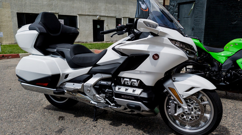A white Honda GOld Wing motorbike from the most recent generation parked at the side of a street.