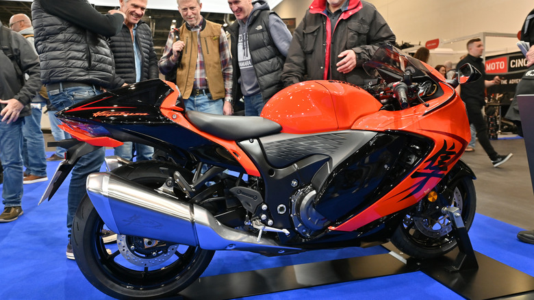 An orange and black Suzuki Hayabusa hyperbike parked on a podium at an indoor bike show with people looking at it.