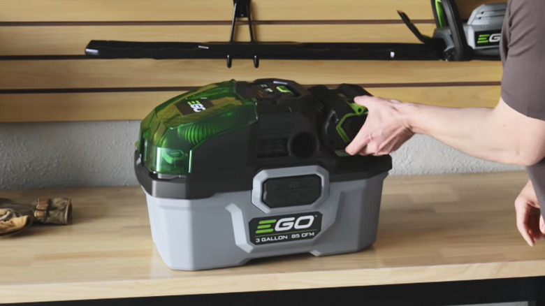 A person changing the battery on a POWER+ 3 Gallon Wet/Dry Vacuum set atop a workbench