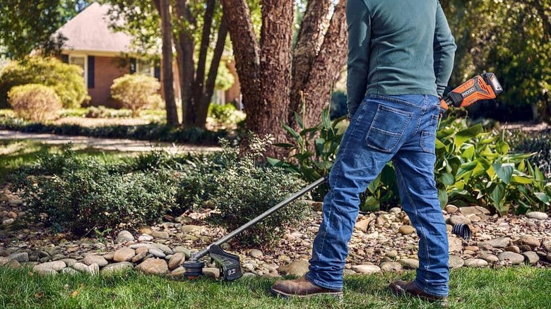 A man uses a Rigid string trimmer on a lawn.