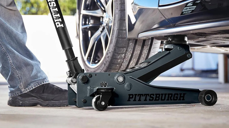 A person using a Pittsburgh floor jack to lift a black car.