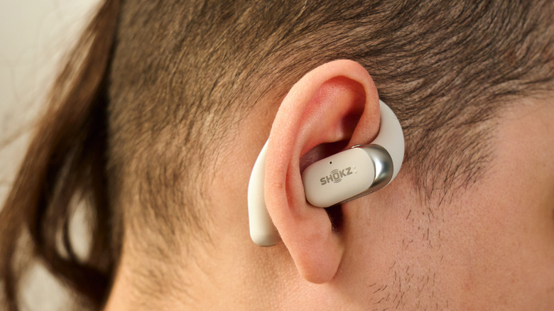 Close-up of a side-shaved head with a white Shokz-brand earphone on his ear