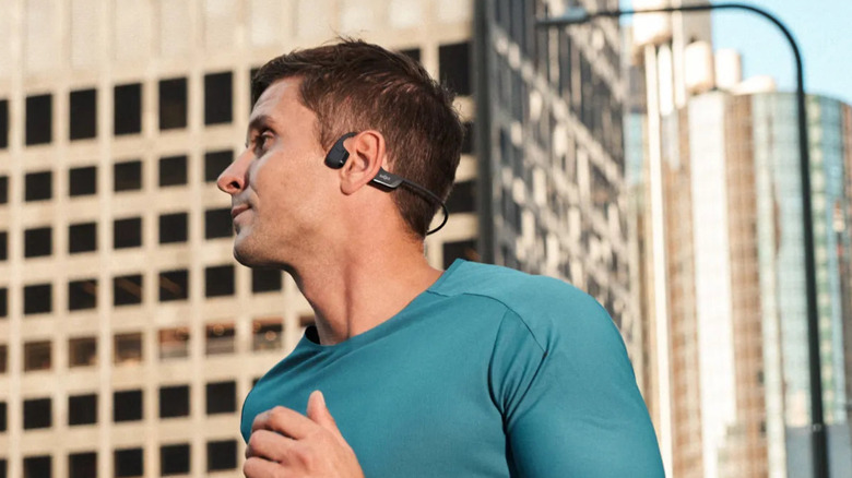 Man in teal shirt running in a city wearing Shokz Open Run Pro 2.