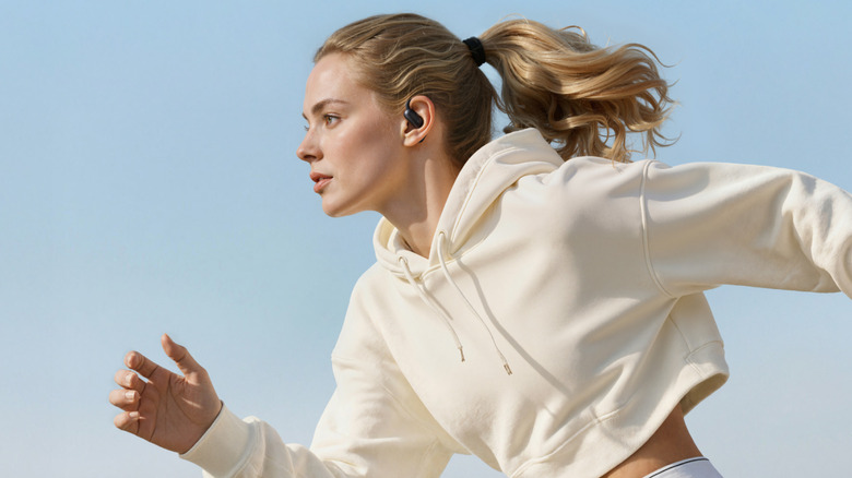 Woman in tan athletic suit running and wearing Soundcore AeroFit 2+.