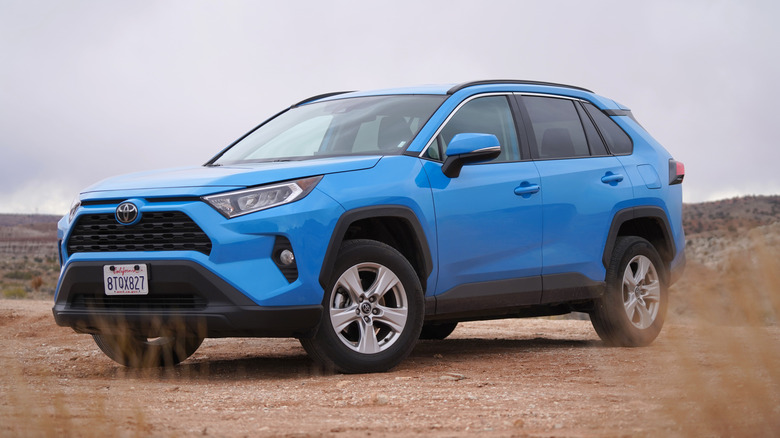 Blue Toyota RAV4 parked on dirt with a cloudy sky behind