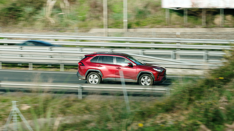 Distant view of a red Toyota RAV4 driving on a freeway with foliage on both sides