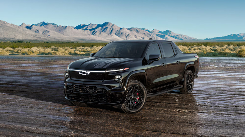 Black Chevrolet Silverado EV on a muddy road with a mountaineous backdrop