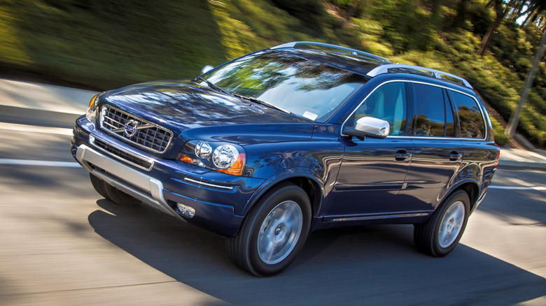 A dark blue 2013 Volvo XC90 traveling at speed up a mountain road, right to left
