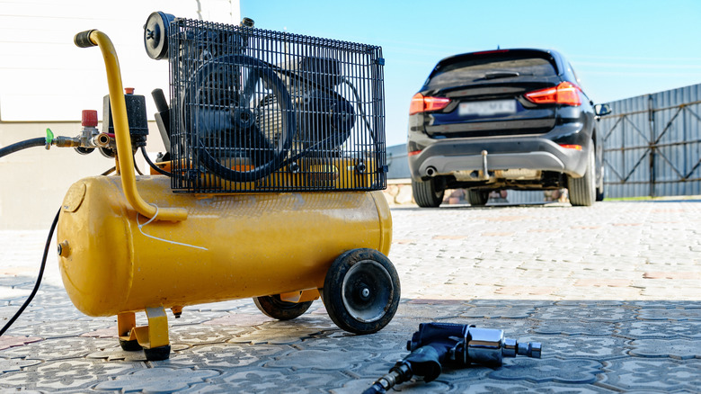 An air compressor in the foreground with a blurry car in the background.